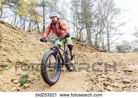 Stock Image - Caucasian man descending dirt trail on bicycle. Fotosearch