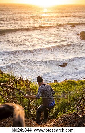 Picture - Caucasian man descending hill near ocean at sunset. Fotosearch