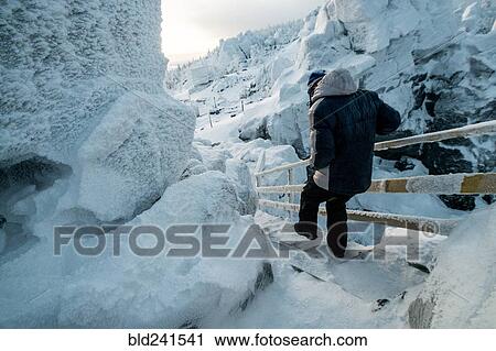 Stock Image - Caucasian man descending snowy staircase near rocks. Fotosearch