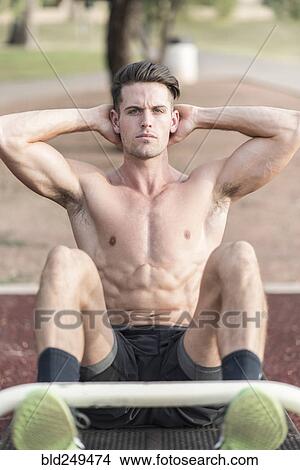 Picture - Caucasian man doing sit-ups outdoors. Fotosearch