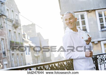 Picture - Caucasian man drinking coffee on the balcony in city. Fotosearch