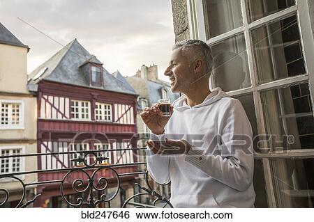 Stock Photograph - Caucasian man enjoying espresso on balcony in city. Fotosearch