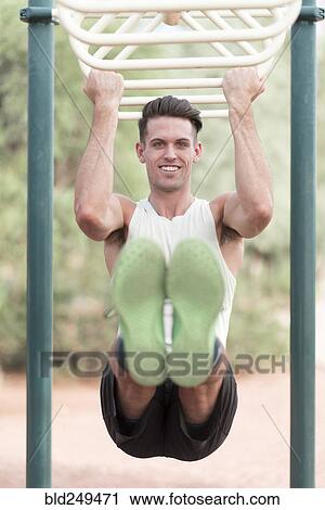 Stock Image - Caucasian man hanging on monkey bars outdoors. Fotosearch