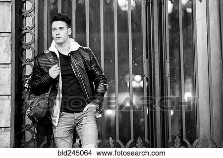 Picture - Caucasian man holding bag leaning on gate. Fotosearch