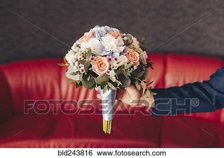 Stock Photograph - Caucasian man holding bouquet of flowers near red sofa. Fotosearch