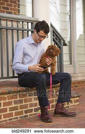Stock Image - Caucasian man holding dog and texting on cell phone. Fotosearch