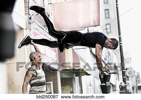 Caucasian man holding leg of friend balancing on parking meter View Large Photo Image Stock Photo - Caucasian man holding leg of friend balancing on parking meter. Fotosearch