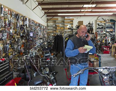 Caucasian man holding notepad near motorcycle talking on cell phone View Large Photo Image Stock Image - Caucasian man holding notepad near motorcycle talking on cell phone. Fotosearch