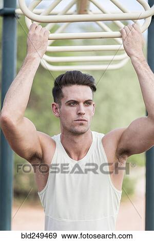 Stock Photo - Caucasian man holding onto monkey bars outdoors. Fotosearch