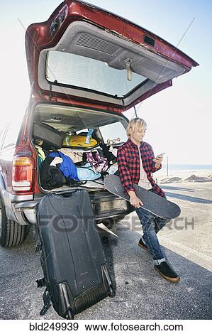 Stock Photo - Caucasian man holding skateboard and texting on cell phone. Fotosearch
