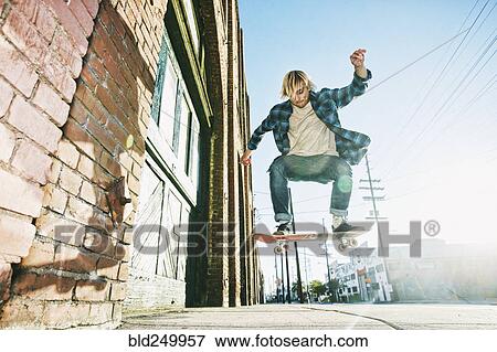 Stock Photo - Caucasian man jumping on skateboard on urban sidewalk. Fotosearch