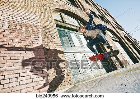 Stock Photograph - Caucasian man jumping on skateboard on urban sidewalk. Fotosearch