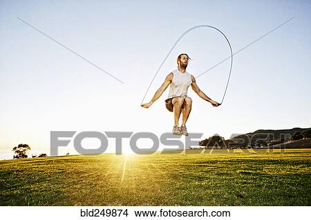 Picture - Caucasian man jumping rope in sunny field. Fotosearch