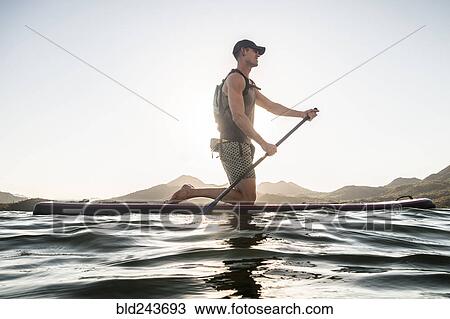 Stock Image - Caucasian man kneeling on paddleboard in river. Fotosearch