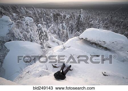 Stock Image - Caucasian man laying in snow texting on cell phone. Fotosearch