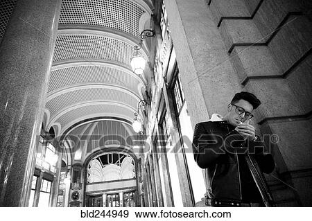 Stock Photo - Caucasian man leaning in wall lighting cigarette. Fotosearch