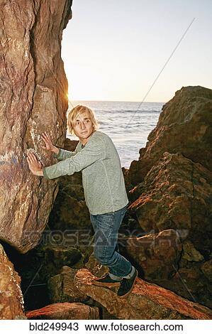 Stock Image - Caucasian man leaning on rocks at ocean. Fotosearch