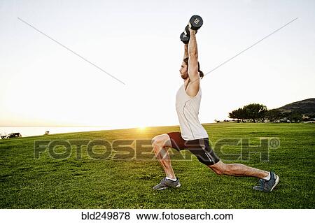 Stock Photo - Caucasian man lifting dumbbells in sunny field. Fotosearch