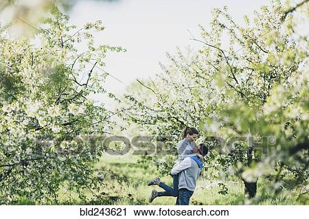 Stock Image - Caucasian man lifting woman under flowering trees. Fotosearch