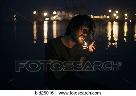 Stock Image - Caucasian man lighting cigarette at waterfront. Fotosearch