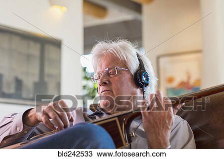 Stock Image - Caucasian man listening to headphones and playing guitar. Fotosearch