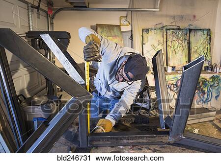 Stock Image - Caucasian man measuring metal sculpture with tape measure. Fotosearch