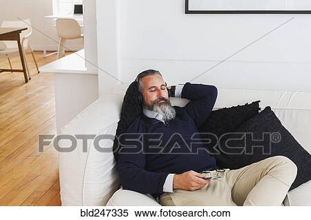 Caucasian man on sofa listening to cell phone with headphones View Large Photo Image Stock Photography - Caucasian man on sofa listening to cell phone with headphones. Fotosearch