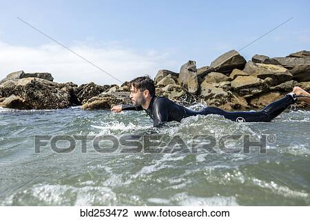 Stock Image - Caucasian man paddling on surfboard. Fotosearch