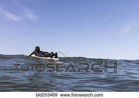 Stock Photo - Caucasian man paddling on surfboard. Fotosearch
