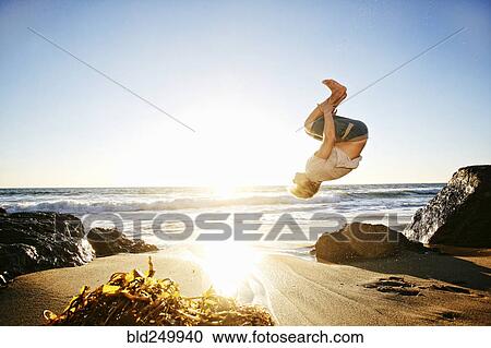 Stock Image - Caucasian man performing backflip on beach. Fotosearch