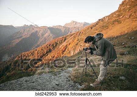 Stock Image - Caucasian man photographing valley from mountain. Fotosearch