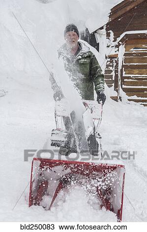 Stock Image - Caucasian man pushing snow blower. Fotosearch