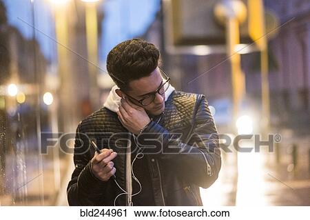 Caucasian man putting earbud in ear outdoors View Large Photo Image Stock Image - Caucasian man putting earbud in ear outdoors. Fotosearch