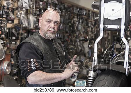 Stock Photograph - Caucasian man repairing motorcycle and wiping hands. Fotosearch