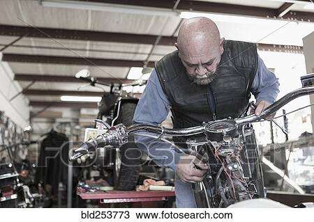 Stock Image - Caucasian man repairing motorcycle. Fotosearch