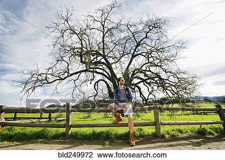 Stock Image - Caucasian man resting on wooden fence. Fotosearch