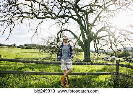 Stock Image - Caucasian man resting on wooden fence. Fotosearch
