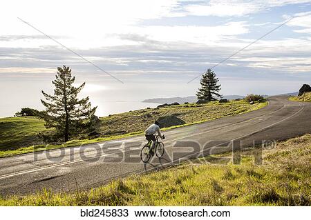 Stock Image - Caucasian man riding bicycle on road near ocean. Fotosearch