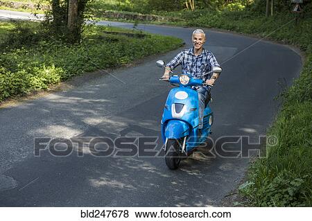 Stock Photo - Caucasian man riding blue motor scooter. Fotosearch