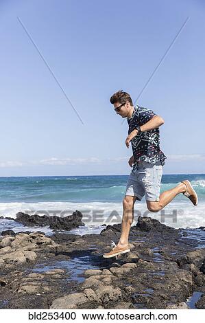 Stock Image - Caucasian man running on rocks on beach. Fotosearch