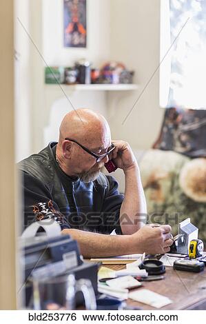 Stock Photograph - Caucasian man sitting at desk talking on cell phone. Fotosearch