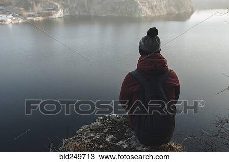 Stock Image - Caucasian man sitting at the edge of reservoir wearing backpack. Fotosearch