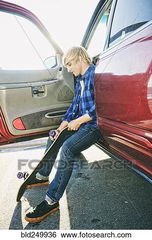 Stock Photograph - Caucasian man sitting in car holding skateboard wheel. Fotosearch