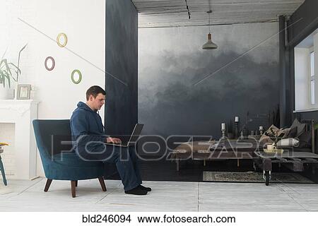 Picture - Caucasian man sitting in chair using laptop. Fotosearch