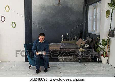 Stock Photography - Caucasian man sitting in chair using digital tablet. Fotosearch