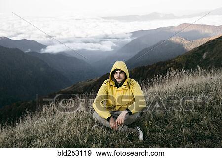 Stock Photo - Caucasian man sitting in remote mountain landscape. Fotosearch