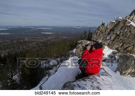 Stock Photography - Caucasian man sitting in snow admiring scenic view of forest. Fotosearch