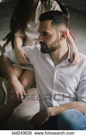 Stock Photography - Caucasian man sitting on floor leaning on woman in chair. Fotosearch
