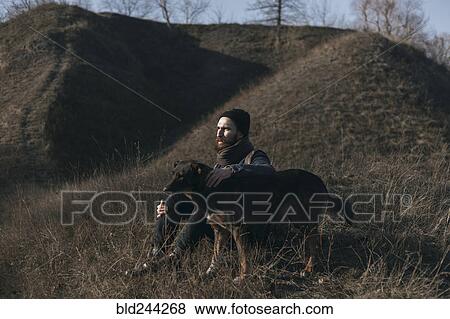 Stock Photo - Caucasian man sitting on hill petting dog. Fotosearch