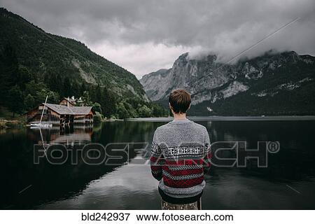 Stock Photo - Caucasian man sitting on post admiring scenic view of mountain. Fotosearch